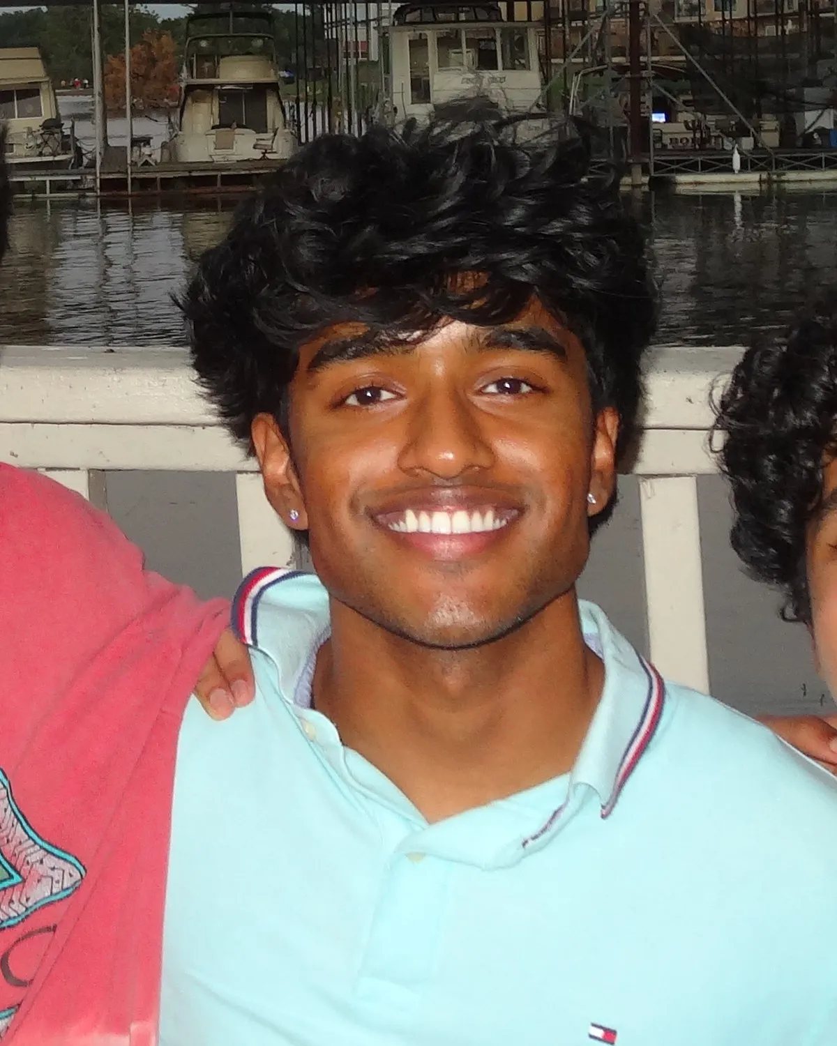 Aman Sriven smiling on a lakeside deck, with boats docked behind him